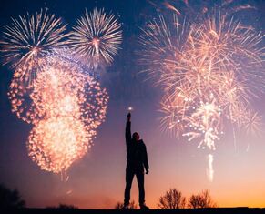 Man raising a sparkler with fireworks bursting overhead | Advanced Therapy Institute of Touch & Falcon Yoga New Year's Eve Rejuvenation Event with Our Medical Massage School Students
