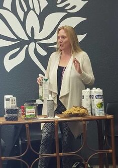 Kim M. Green, Founder of Advanced Therapy institute of Touch showing how to make a heart healthy drink with coconut water, chia seeds, almond milk and cinnamon.  Standing in front of a small table with all the ingredients present.
